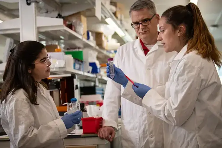 CMU students and professor wearing gloves and labcoats in a chemistry lab.