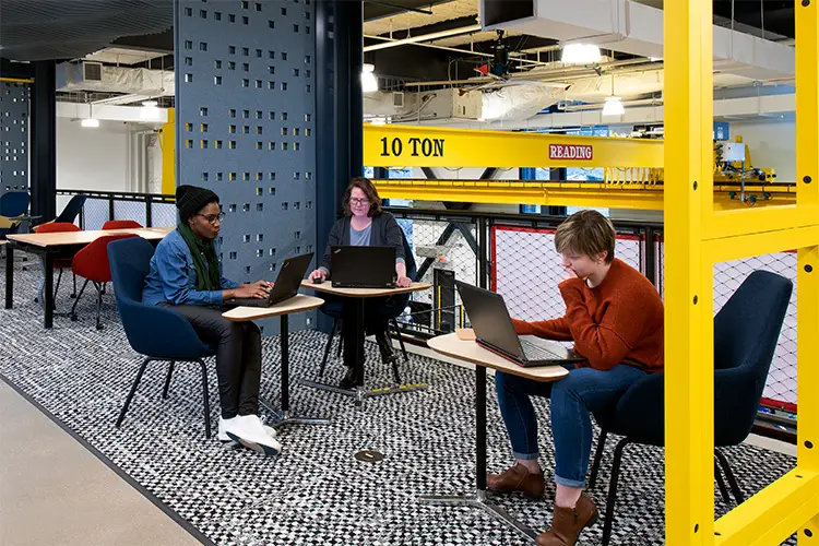 Three people working in a common space on laptops.