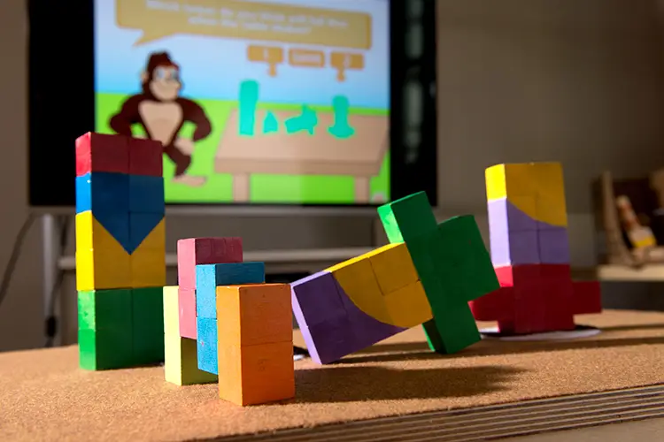 Building blocks on an interactive table in front of a screen with a gorilla.