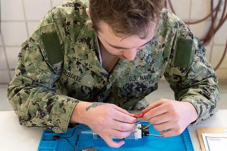Naval sailor adjusting wiring for a robotic component in Carnegie Mellon Robotics Academy.